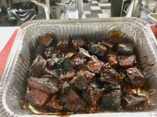 A tray of dark, caramelized meat cubes, likely barbecue, with a glossy sauce, set in a kitchen environment.