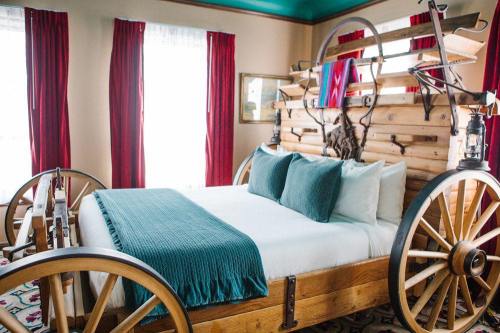 A unique bedroom featuring a bed designed like a wagon, with teal pillows and red curtains.