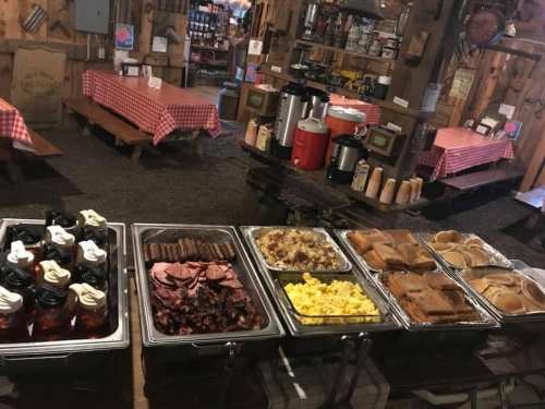 A buffet spread featuring various meats, scrambled eggs, and desserts in a rustic dining setting with checkered tablecloths.