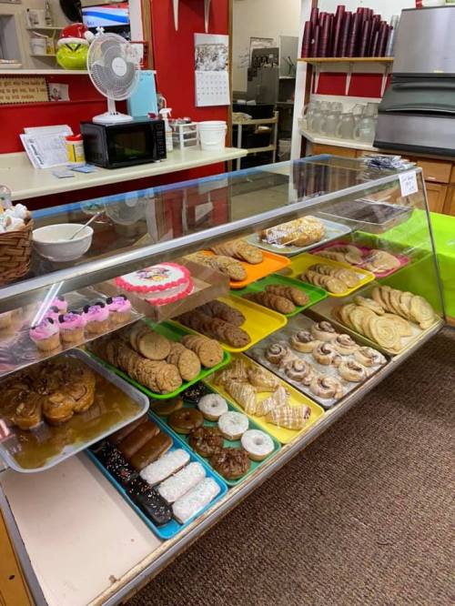 A display case filled with various baked goods, including cookies, pastries, and cupcakes in a cozy bakery setting.