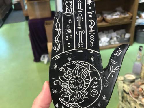 A decorative black hand-shaped object with intricate white designs, including a sun and various symbols.