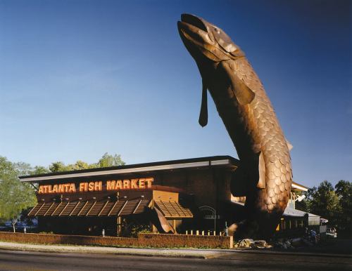 A large fish sculpture stands in front of the Atlanta Fish Market restaurant, showcasing its seafood theme.