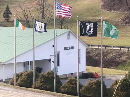 A white building with a green roof, displaying multiple flags, including the American and Irish flags, in a rural setting.