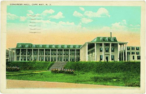 Historic Congress Hall in Cape May, NJ, featuring a large building with green roofs and a grassy foreground.