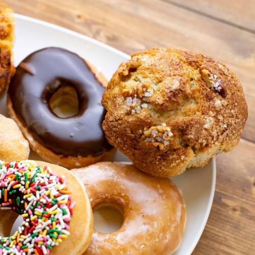 A plate of assorted donuts, including a chocolate frosted, glazed, and a sprinkle-covered donut, alongside a muffin.