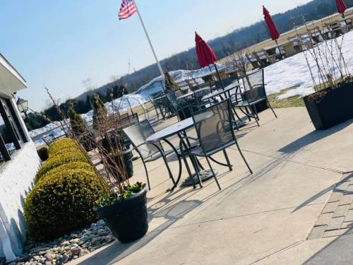 Outdoor seating area with tables, chairs, and planters, featuring a flag and snow in the background.