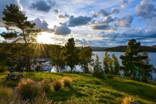 A serene lakeside view at sunset, with trees, clouds, and a picnic area in the foreground.
