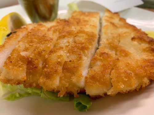 Crispy, golden-brown breaded fish fillet served on a bed of lettuce with a lemon wedge in the background.