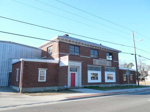 A two-story brick building with a red door, large windows, and a sign, set against a clear blue sky.