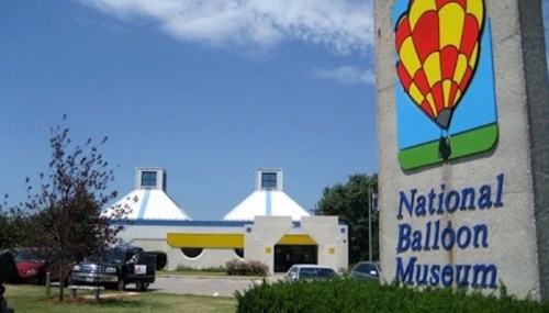 Sign for the National Balloon Museum with a modern building and blue sky in the background.