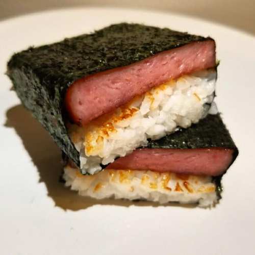 Two stacked pieces of sushi made with rice, seaweed, and a layer of pink spam.