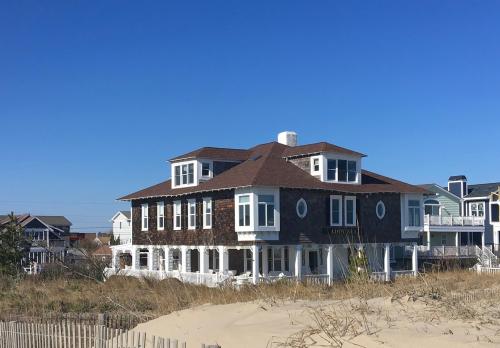 A large beach house with multiple windows, surrounded by sand dunes and a clear blue sky.