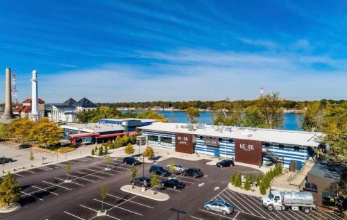 Aerial view of a waterfront building with a lighthouse, surrounded by trees and parked cars. Clear blue sky above.