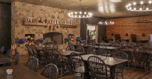 Cozy dining room with wooden tables, black chairs, a stone fireplace, and decorative flowers on the tables.