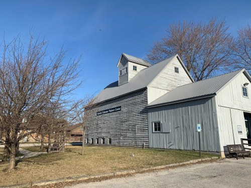 A gray wooden building with a peaked roof, surrounded by bare trees and a clear blue sky.