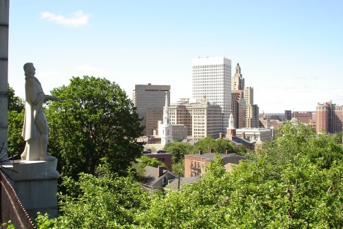 A city skyline with modern buildings and greenery in the foreground, featuring a statue overlooking the scene.