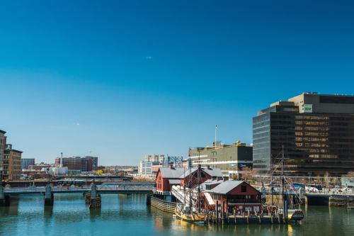 A scenic view of a harbor with historic buildings, boats, and modern skyscrapers under a clear blue sky.