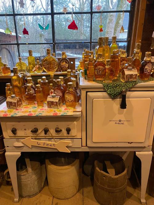 A vintage stove adorned with various bottles of honey and syrup, set against a window with colorful decorations.