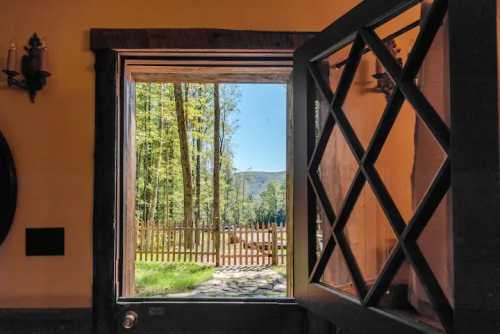 View from an open door showcasing a sunny outdoor scene with trees and a wooden fence.