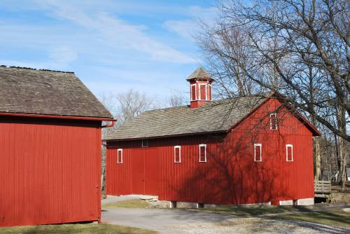 A red barn with a cupola, surrounded by trees and a clear blue sky, showcasing a rural landscape.