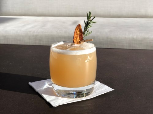 A refreshing cocktail in a glass, garnished with a dried fruit slice and a sprig of rosemary, on a napkin.