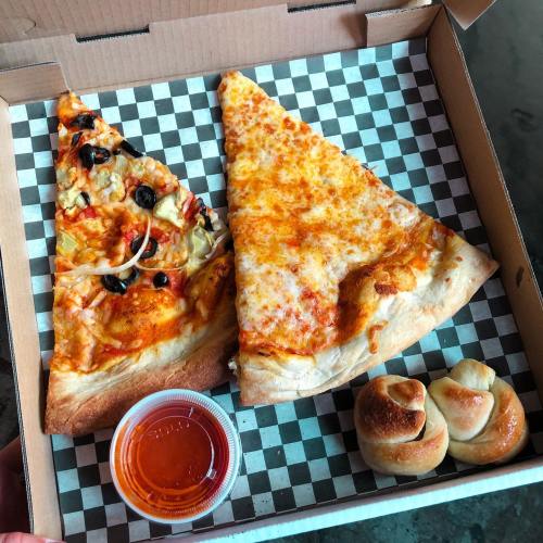 A pizza box containing two slices of pizza—one with olives and onions, the other plain cheese—and a side of breadsticks.