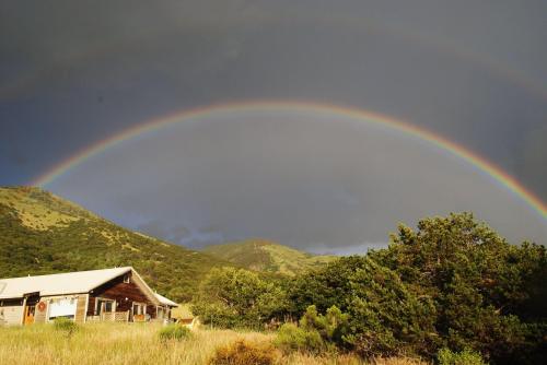A vibrant double rainbow arcs over a rustic cabin surrounded by lush greenery and rolling hills.