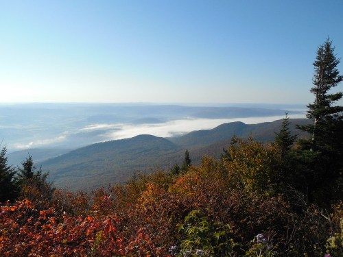 A scenic view of mountains with colorful autumn foliage and a misty valley below under a clear blue sky.