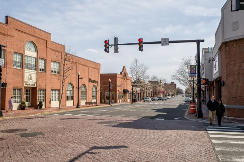 A quiet street scene with brick buildings, traffic lights, and pedestrians crossing on a sunny day.