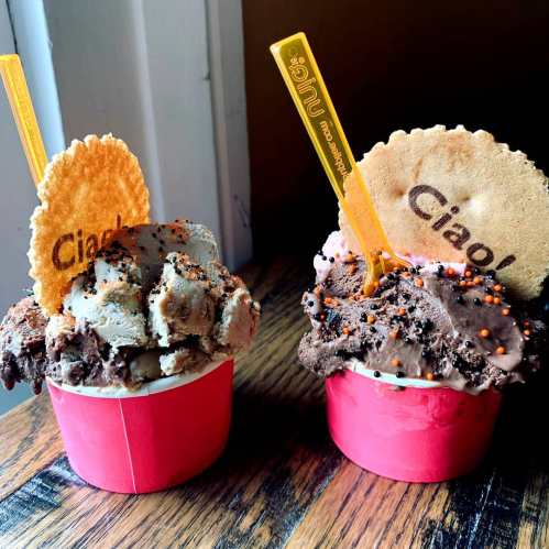 Two colorful ice cream cups with chocolate and cookie dough flavors, topped with sprinkles and wafer cookies.