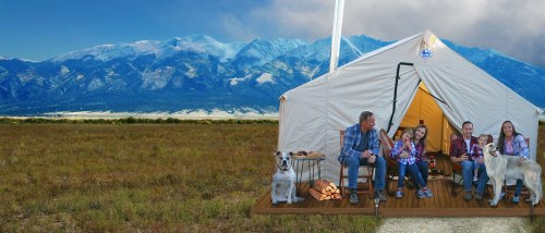 A family sits outside a tent in a scenic mountain landscape, enjoying time with their dogs and a campfire.