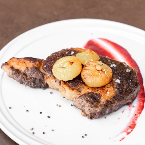 A perfectly cooked steak topped with caramelized onions, served on a white plate with a red sauce drizzle.