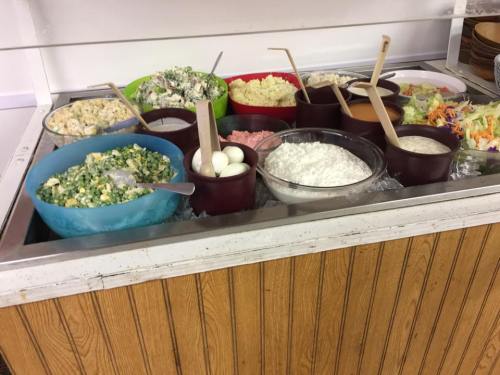 A variety of colorful salads and dishes in bowls, including greens, eggs, and creamy sides, displayed on a counter.