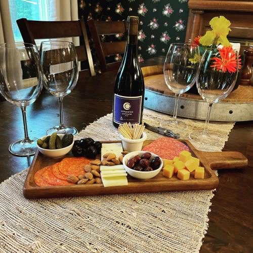 A wooden charcuterie board with meats, cheeses, olives, and nuts, alongside a bottle of wine and wine glasses.