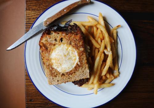 A plate with a toasted sandwich topped with an egg and a side of crispy fries, accompanied by a knife.
