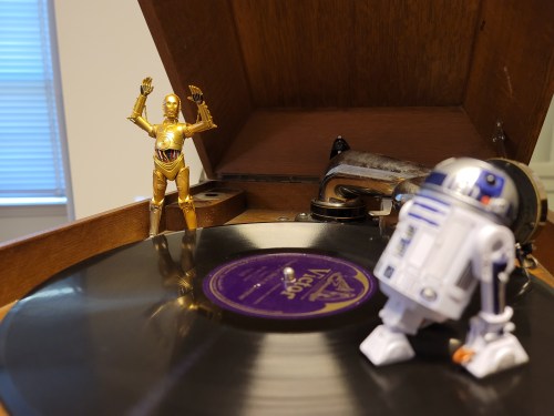 A vintage record player with a vinyl record, featuring C-3PO and R2-D2 action figures.