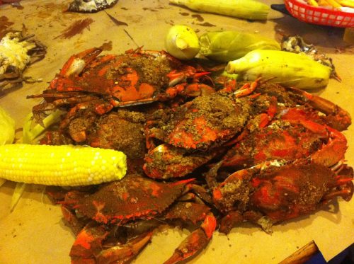 A pile of seasoned crabs with corn on the cob, resting on brown paper.