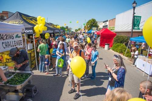 A bustling street market filled with people, colorful tents, and yellow balloons on a sunny day.
