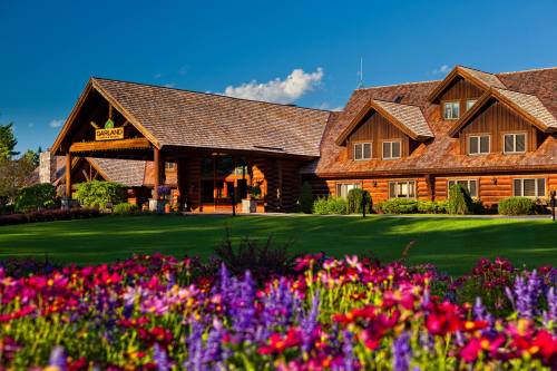A rustic lodge with a wooden exterior surrounded by colorful flowers and a clear blue sky.