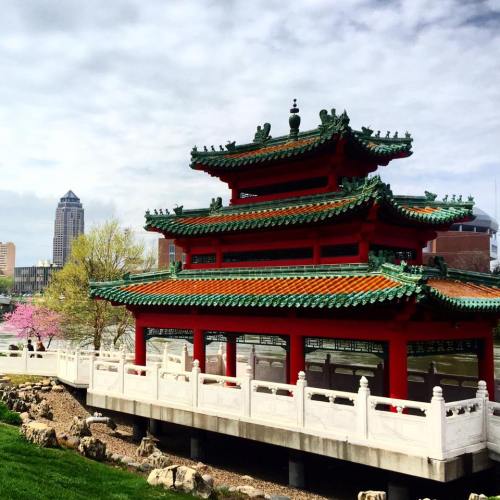 A traditional Chinese pagoda with green and red roofs, surrounded by greenery and a city skyline in the background.