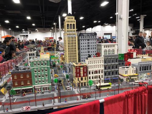 A detailed LEGO city display featuring buildings, streets, and mini-figures, with a crowd in the background.