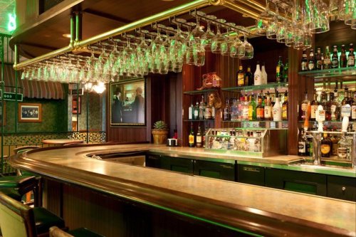 A well-lit bar with a polished counter, hanging glasses, and a variety of liquor bottles on shelves behind it.