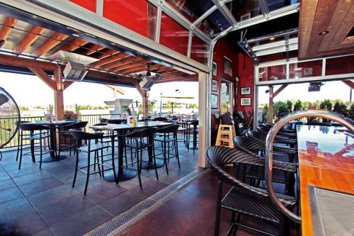Interior of a modern bar with open garage doors, featuring high tables and chairs, wooden beams, and a sleek bar counter.