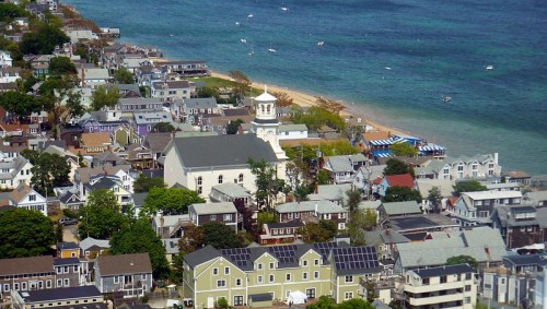 Aerial view of a coastal town with colorful houses, a church, and a beach along the blue water.