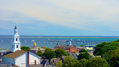 A scenic view of a coastal town with boats in the water, colorful buildings, and a church steeple in the foreground.