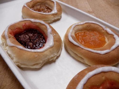A tray of four sweet pastries with fruit fillings and icing, featuring flavors like cherry, raspberry, and orange.
