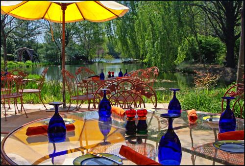 A sunny outdoor dining area by a serene lake, featuring blue glassware and orange napkins on a glass table.