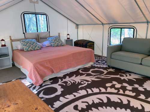 Cozy glamping tent interior with a bed, sofa, and decorative rug, surrounded by nature.