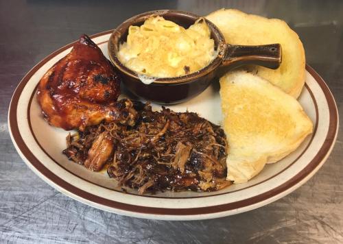 A plate featuring grilled chicken, pulled pork, macaroni and cheese, and two slices of toasted bread.