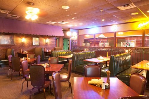 Cozy restaurant interior with booths, tables, and warm lighting, featuring brick walls and colorful decor.